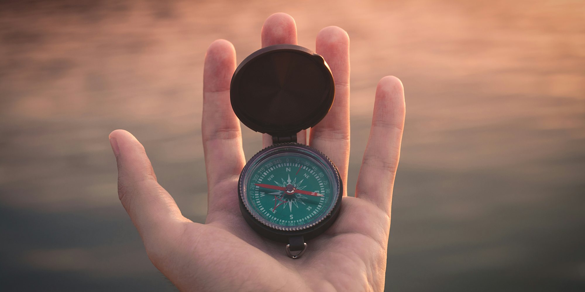 An open hand holding a compass at dusk.