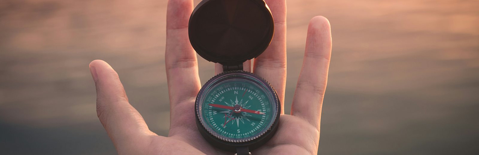 An open hand holding a compass at dusk.