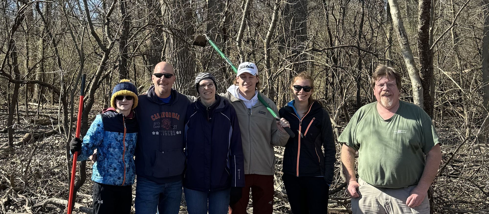Aric with a group from The Intentional Dad community, standing together in the spring woods with rakes after a work day